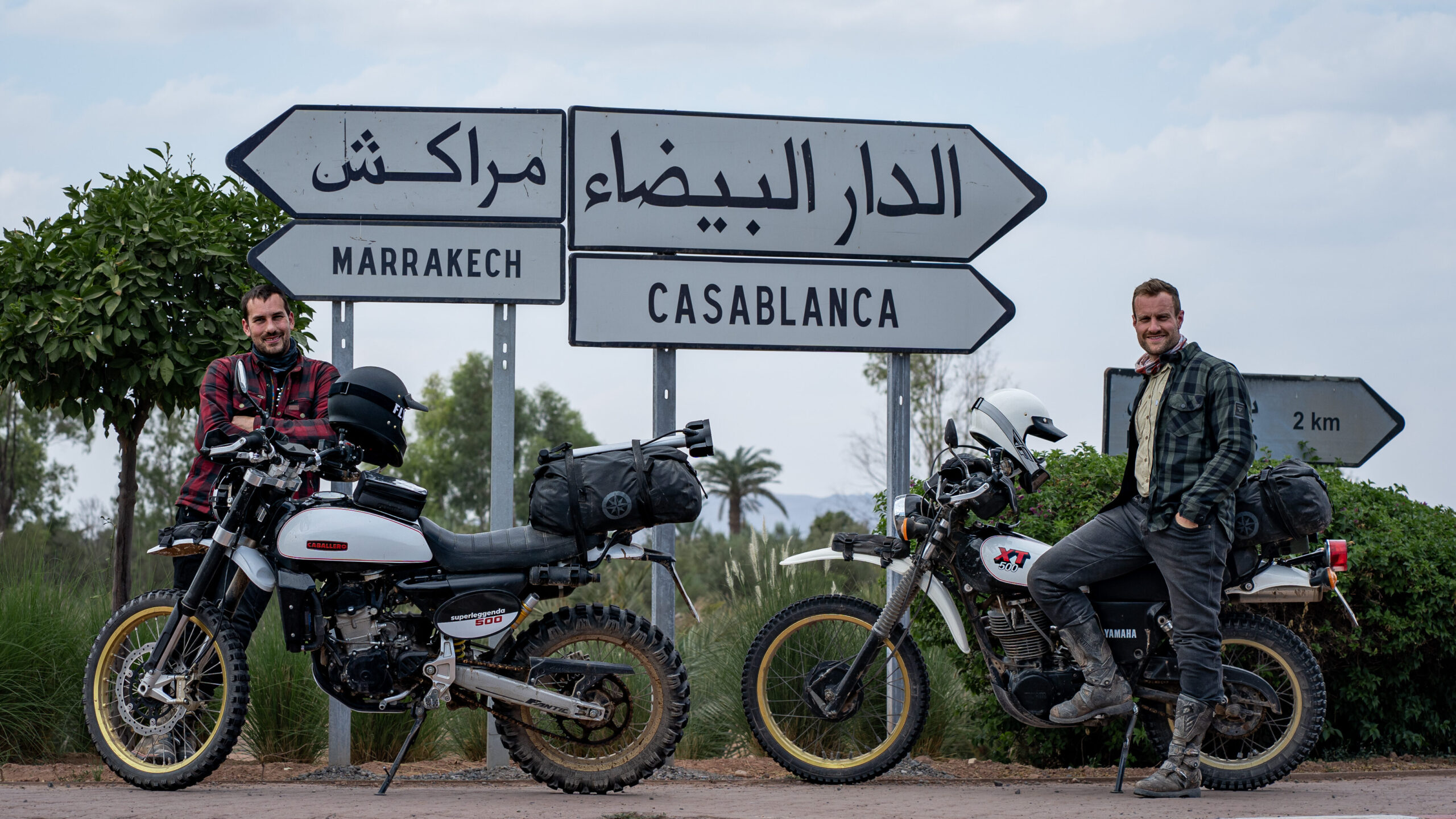 Matthias und Johannes mit zwei Motorrädern vor einem Wegweiser nach Marrakech